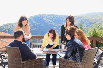 A group of people are sitting on the balcony and a woman is drawing on the table